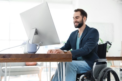 Photo of Young man in wheelchair using computer at workplace