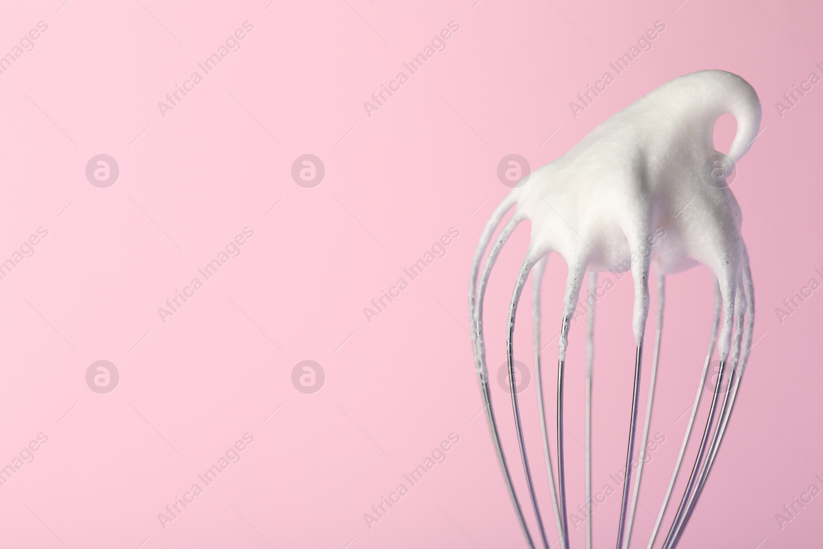 Photo of Whisk with whipped egg whites on pink background, closeup