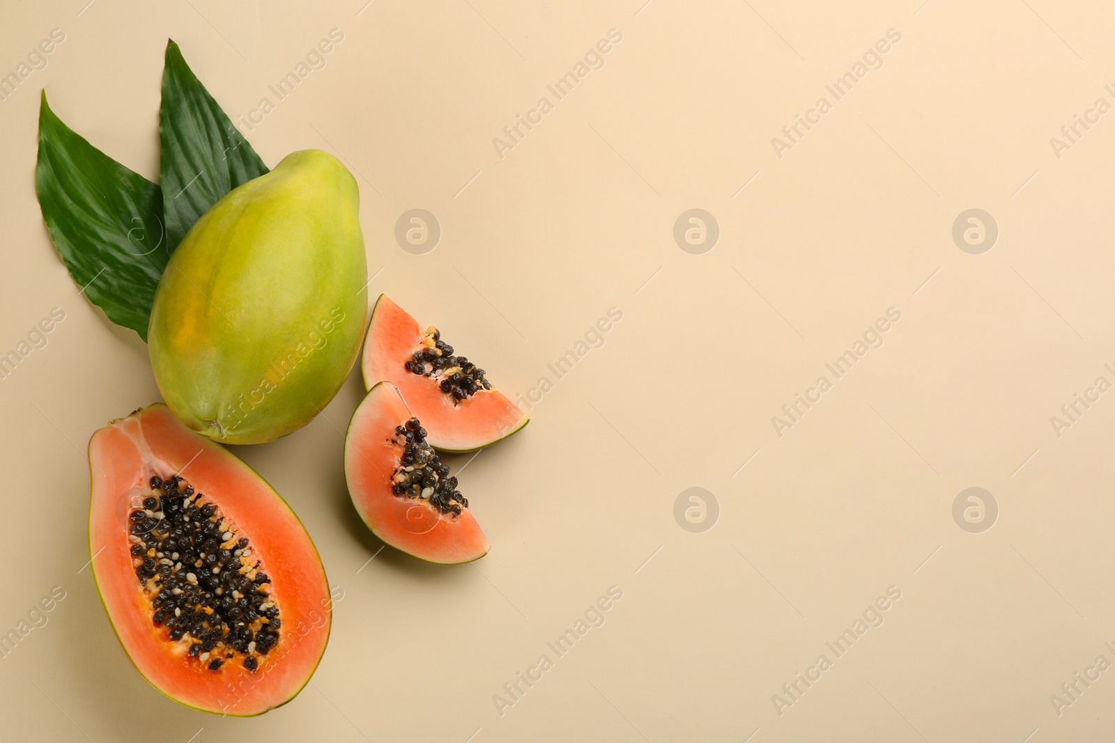 Photo of Fresh ripe papaya fruits with green leaves on beige background, flat lay. Space for text