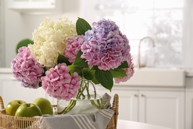 Photo of Bouquet of beautiful hydrangea flowers and apples in kitchen, closeup. Interior design element