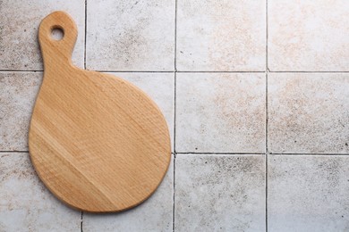 Photo of Wooden cutting board on tiled table, top view. Space for text