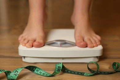 Photo of Overweight girl using scales near measuring tape on wooden floor, selective focus