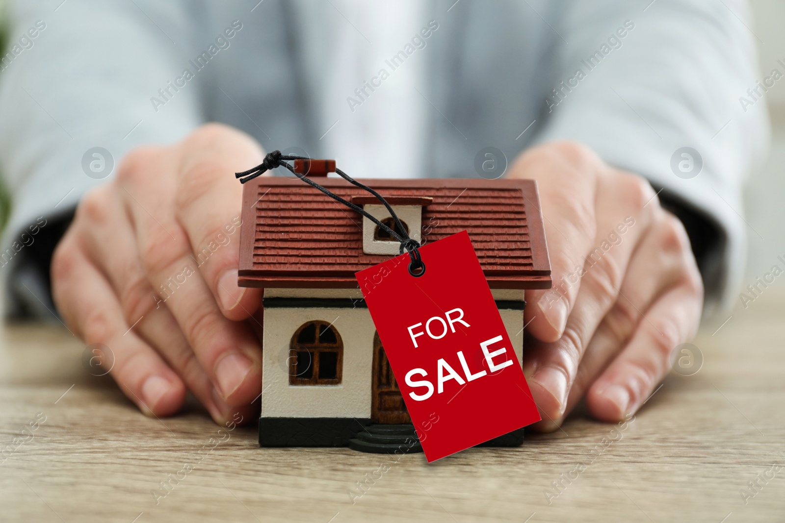 Image of Real estate agent holding house model with SALE label at wooden table, closeup