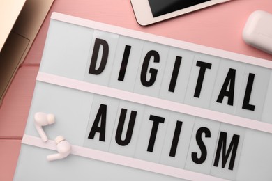Photo of Lightbox with phrase Digital Autism and devices on pink wooden table, flat lay