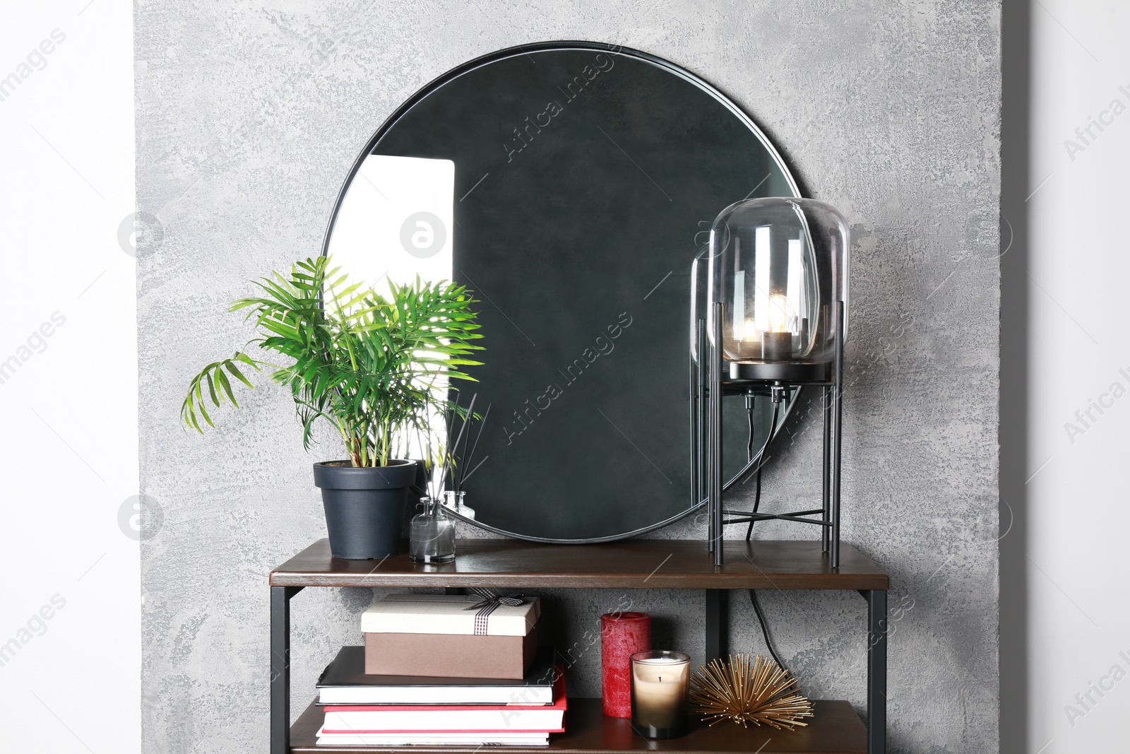 Photo of Stylish round mirror, lamp and houseplant on stand indoors. Interior design