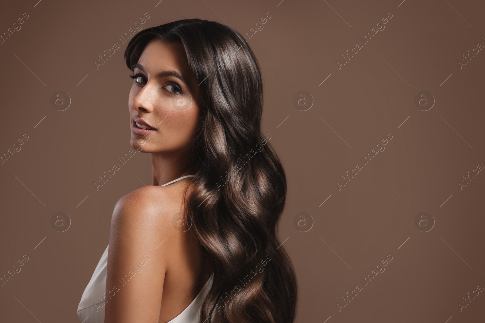 Image of Gorgeous woman with shiny wavy hair on brown background, space for text. Professional hairstyling