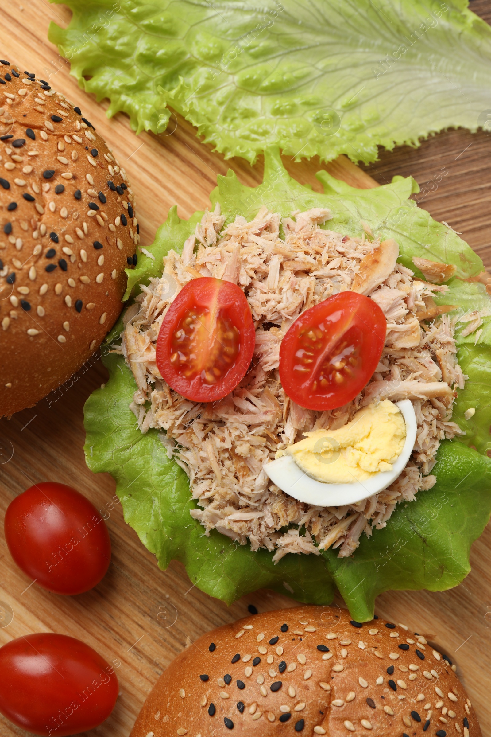 Photo of Delicious sandwich with tuna, boiled egg and vegetables on wooden board, flat lay