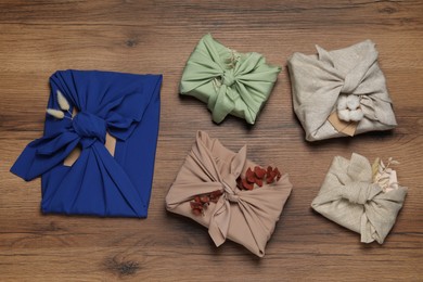 Photo of Furoshiki technique. Many gifts packed in fabric and dry leaves on wooden table, flat lay