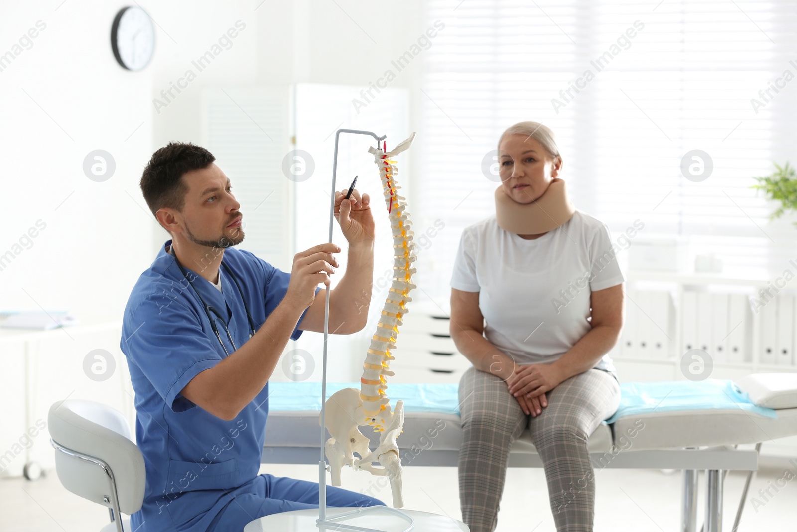 Photo of Male orthopedist explaining structure of spine to patient in clinic