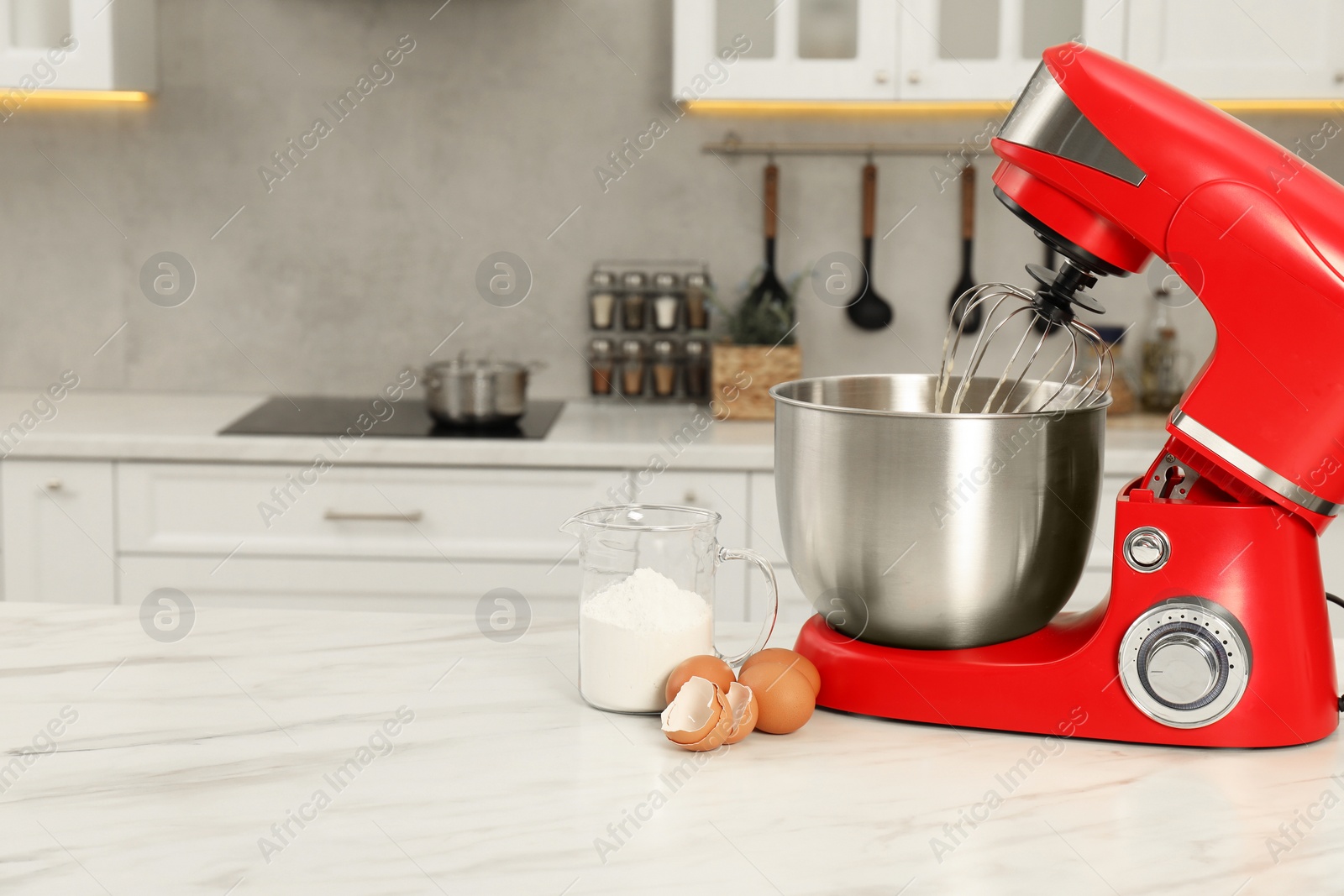 Photo of Modern red stand mixer, eggs and container with flour on white marble table in kitchen, space for text