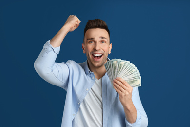 Emotional man with cash money on blue background