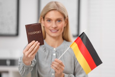 Photo of Immigration. Happy woman with passport and flag of Germany indoors, selective focus