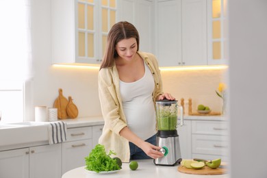 Photo of Young pregnant woman preparing smoothie at table in kitchen. Healthy eating