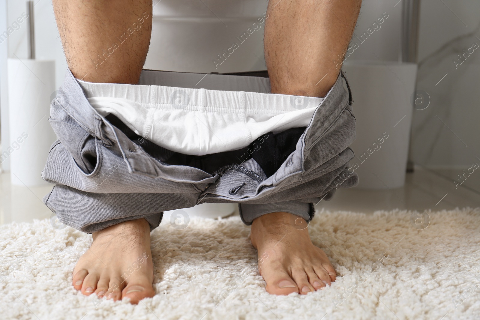 Photo of Man sitting on toilet bowl in bathroom, closeup