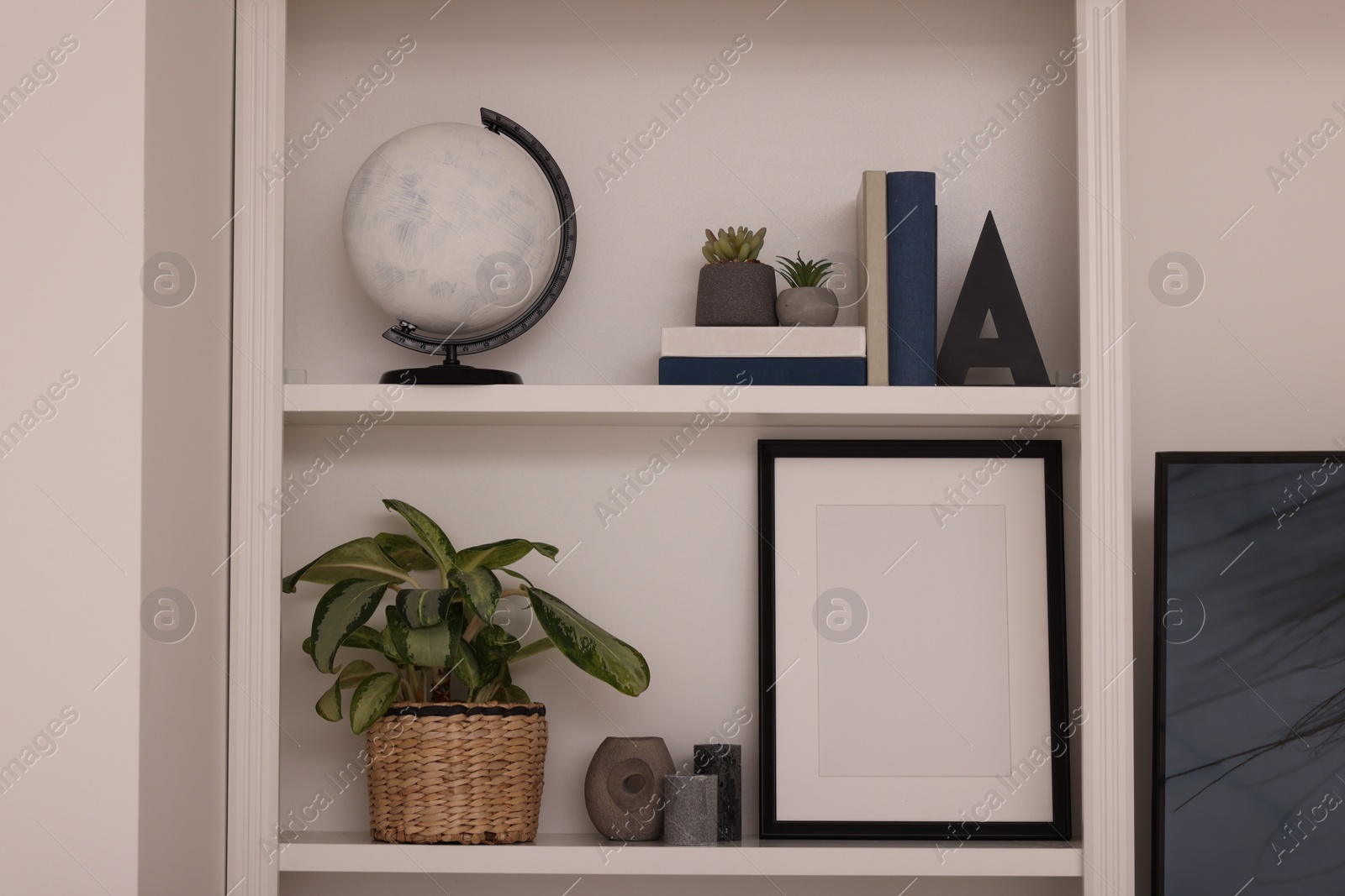 Photo of Interior design. Shelves with stylish accessories, potted plants and frame near white wall