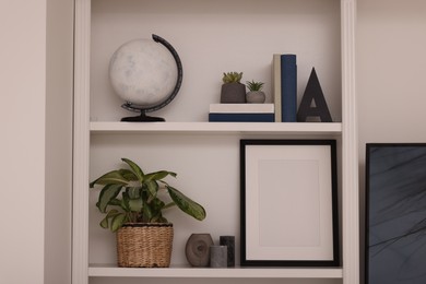 Photo of Interior design. Shelves with stylish accessories, potted plants and frame near white wall