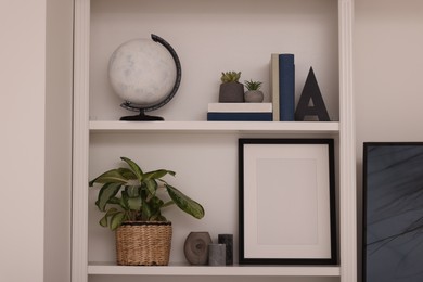 Interior design. Shelves with stylish accessories, potted plants and frame near white wall