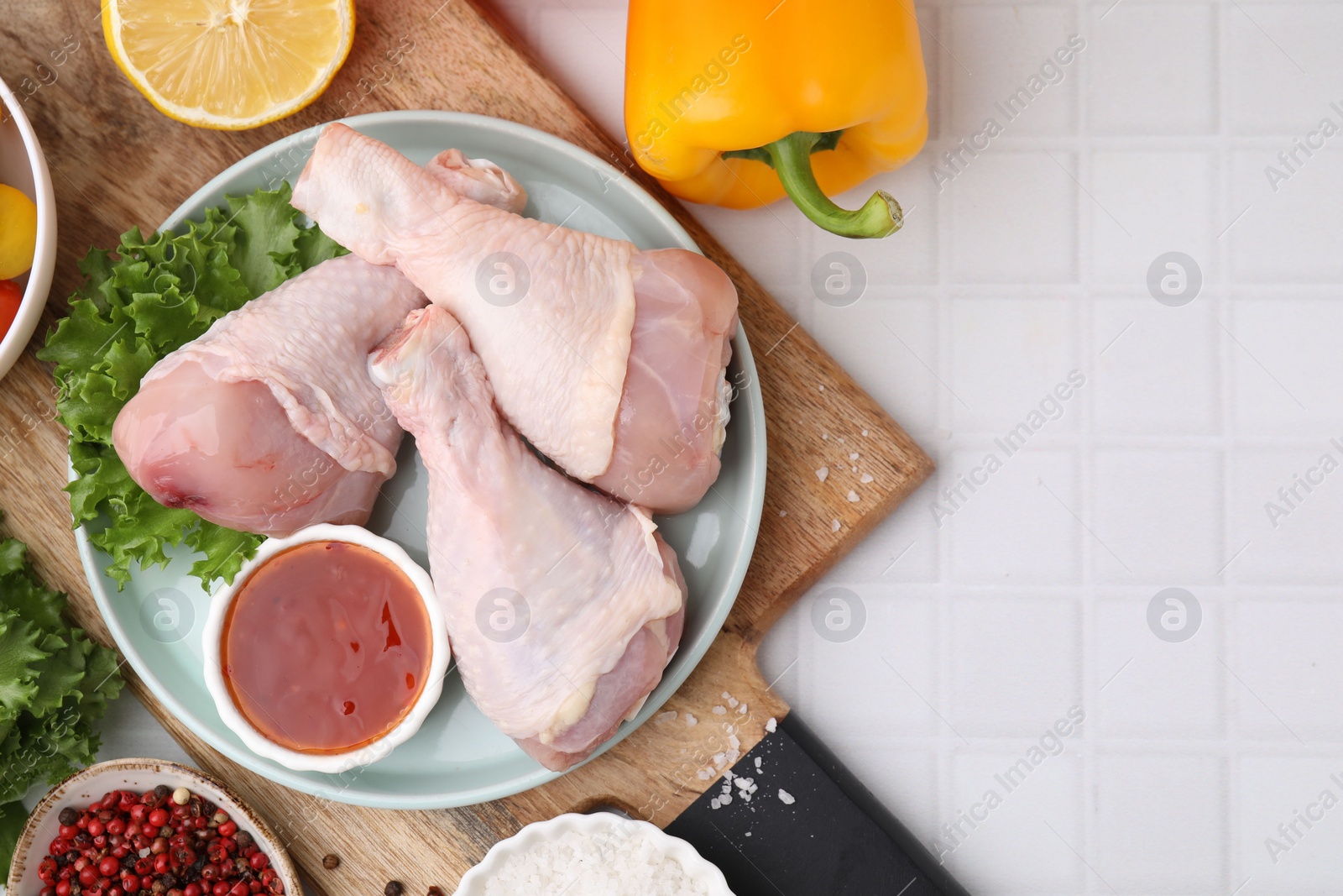 Photo of Flat lay composition with marinade and raw chicken drumsticks on white tiled table. Space for text