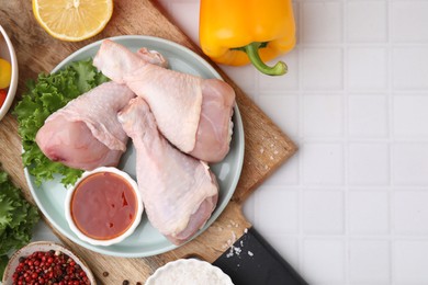 Flat lay composition with marinade and raw chicken drumsticks on white tiled table. Space for text