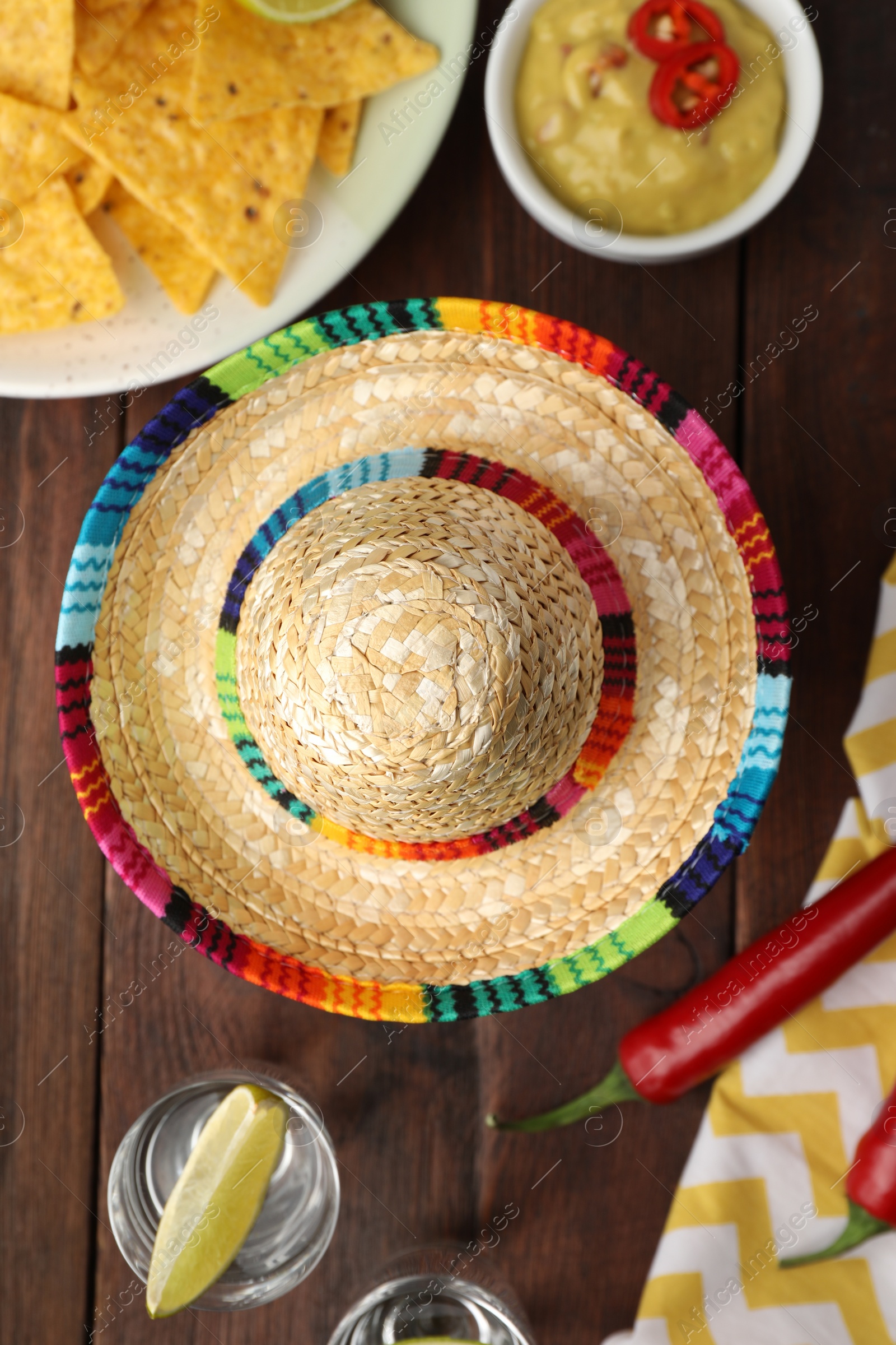 Photo of Mexican sombrero hat, tequila with lime, chili peppers, nachos chips and dip sauce on wooden table, flat lay