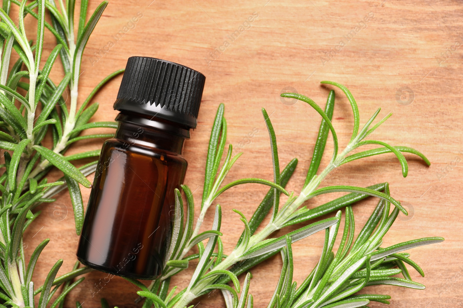 Photo of Bottle of essential oil and fresh rosemary on wooden table, flat lay