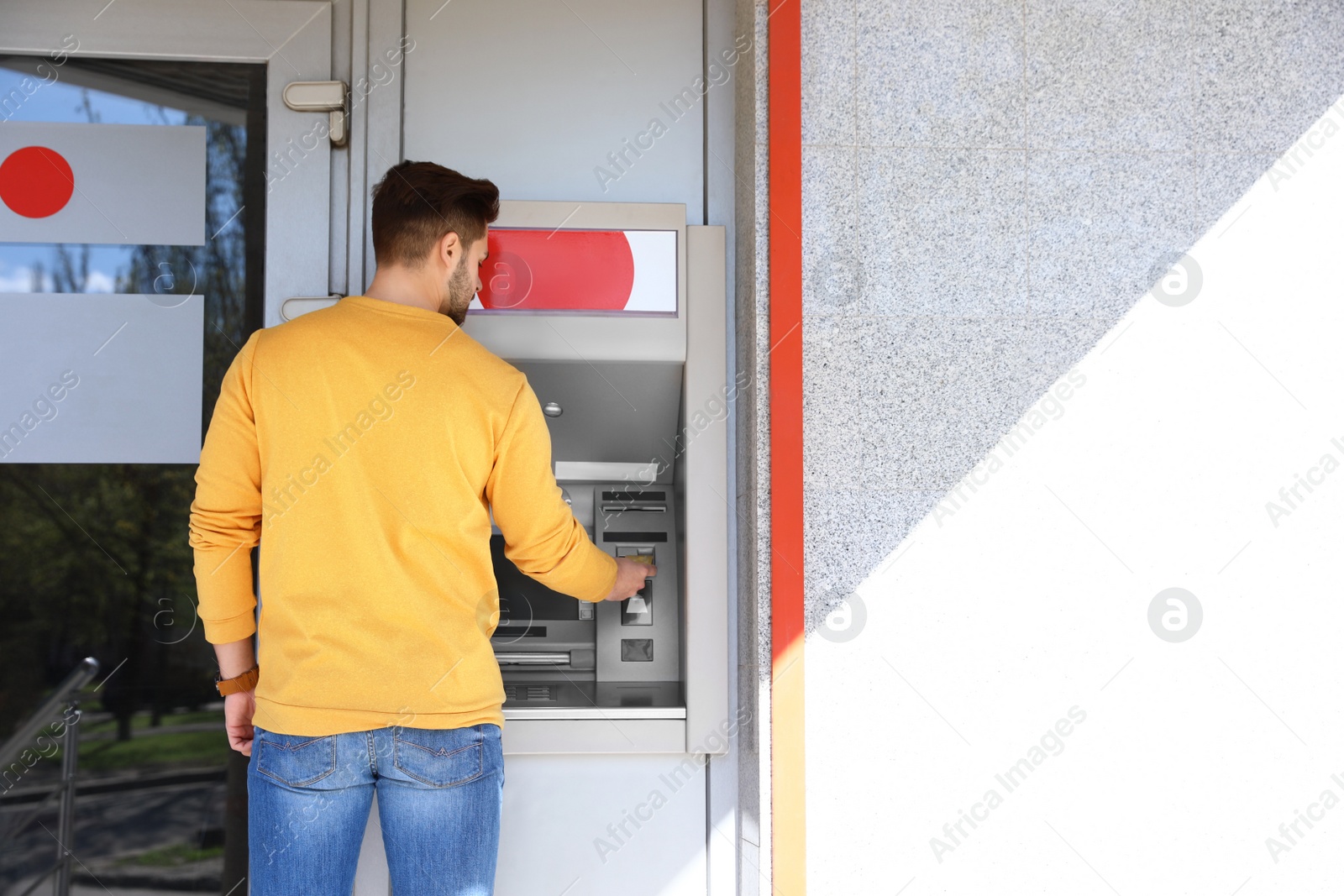 Photo of Young man using modern cash machine outdoors