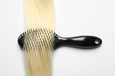 Photo of Stylish brush with blonde hair strand on white background, top view