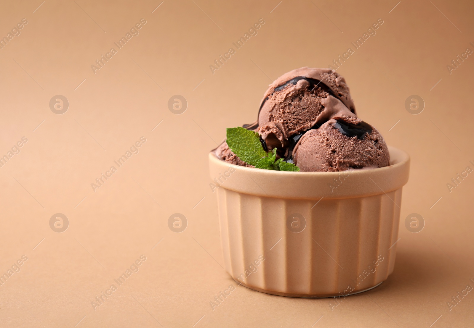 Photo of Bowl of tasty chocolate ice cream with mint on beige background, space for text