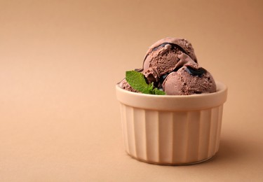 Bowl of tasty chocolate ice cream with mint on beige background, space for text