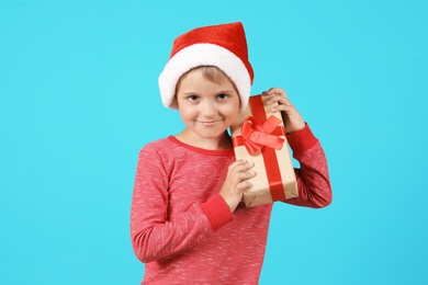 Photo of Cute little child in Santa hat with Christmas gift on color background