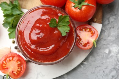 Photo of Delicious ketchup in bowl, parsley and tomatoes on grey textured table, top view