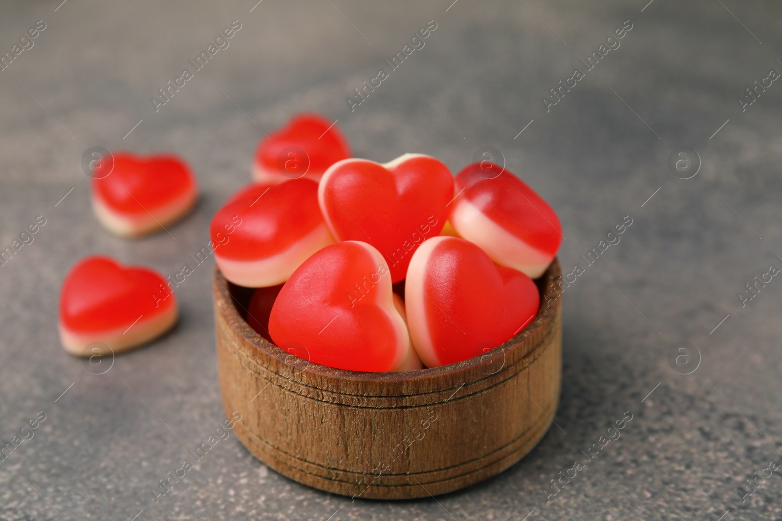 Photo of Bowl and delicious heart shaped jelly candies on brown table, closeup