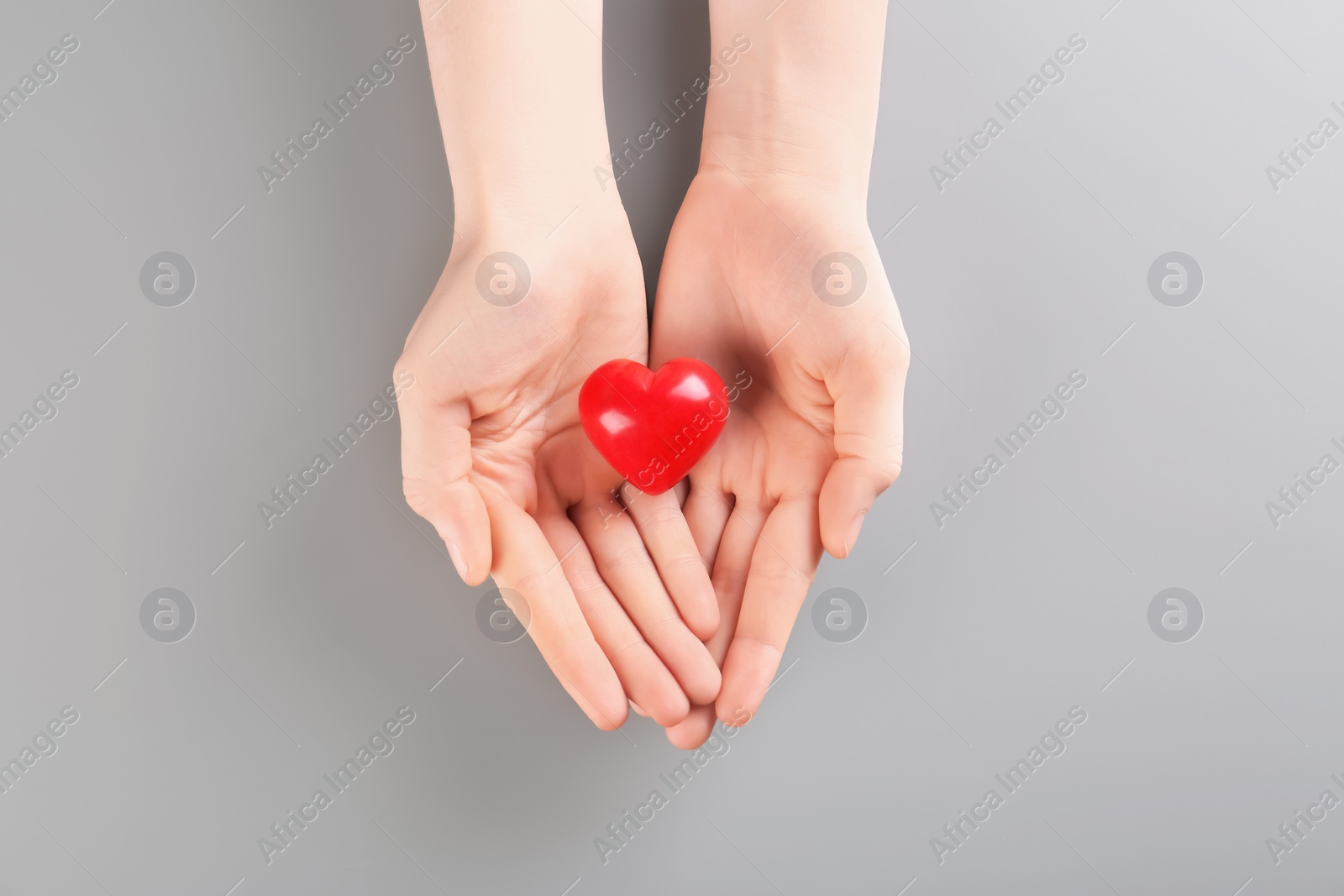 Photo of Woman holding small red heart on gray background. Heart attack concept