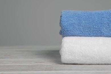 Photo of Soft folded towels on white wooden table against light grey background, space for text