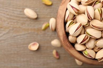 Tasty pistachios in bowl on wooden table, top view. Space for text