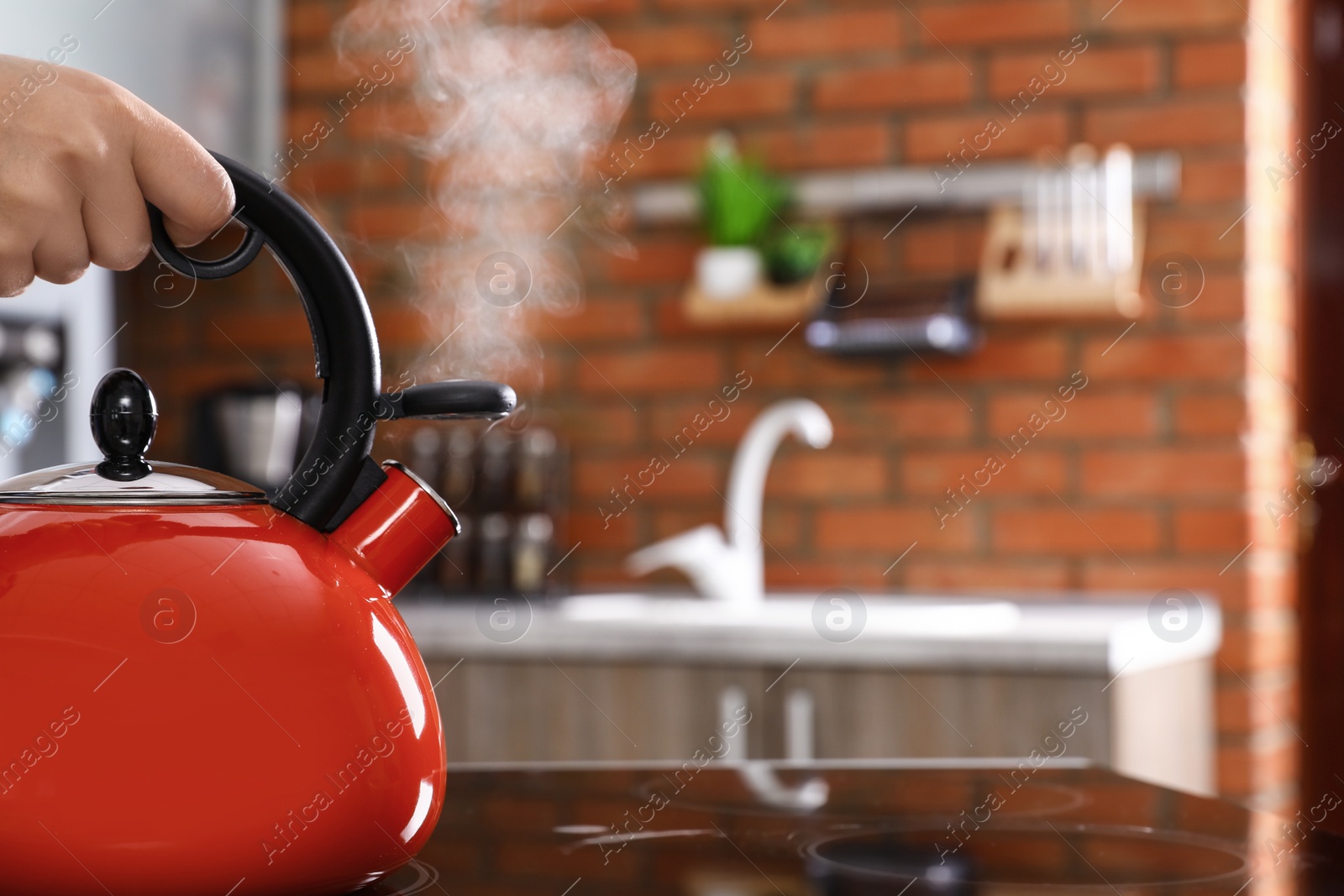 Photo of Woman holding modern kettle on stove in kitchen, closeup with space for text