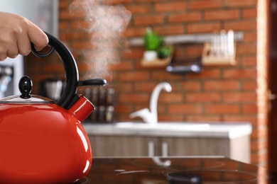 Photo of Woman holding modern kettle on stove in kitchen, closeup with space for text