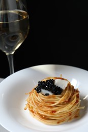 Photo of Tasty spaghetti with tomato sauce and black caviar on plate against dark background, closeup. Exquisite presentation of pasta dish