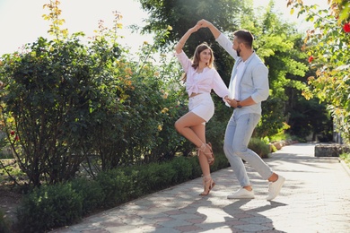 Lovely young couple dancing together in park on sunny day