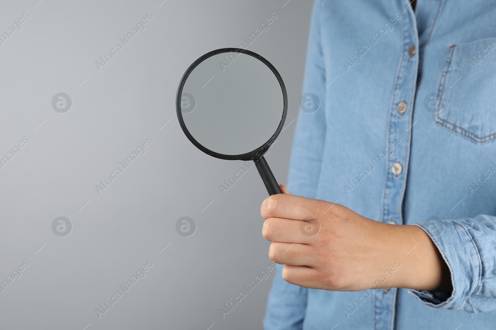 Photo of Woman holding magnifying glass on grey background, closeup. Find keywords concept