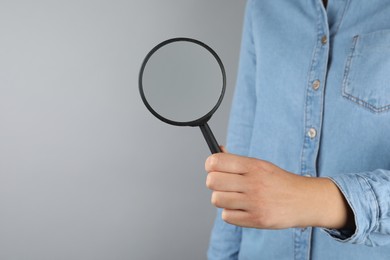 Photo of Woman holding magnifying glass on grey background, closeup. Find keywords concept