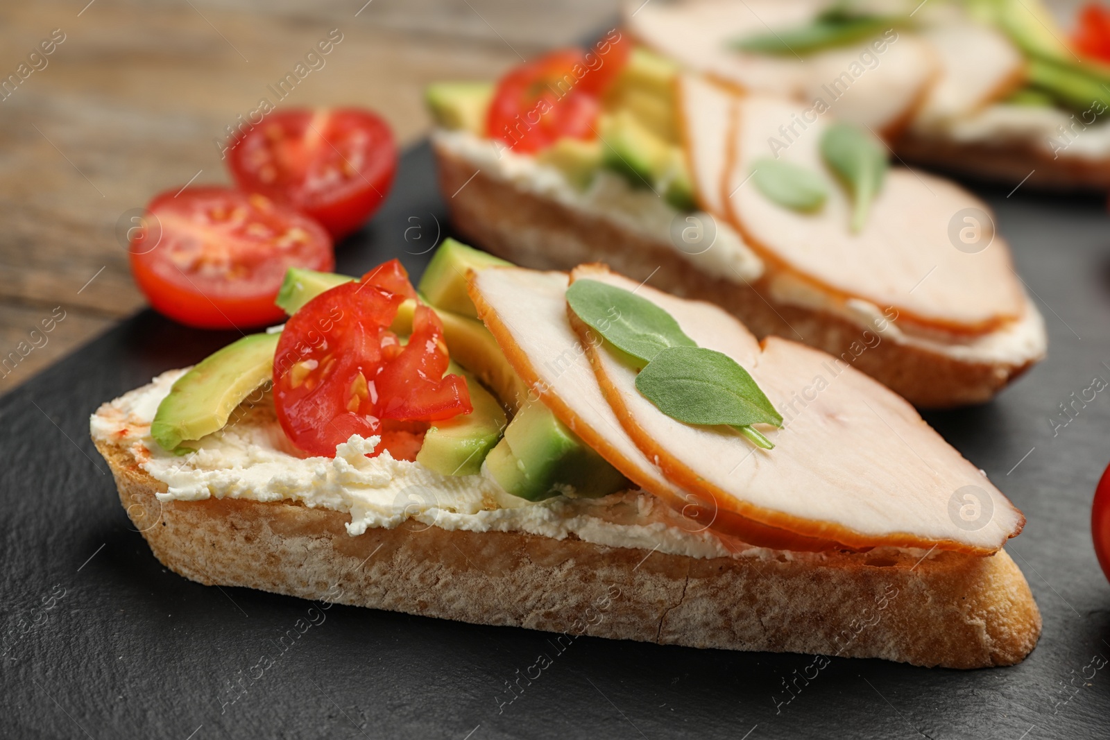 Photo of Delicious chicken bruschettas on slate plate, closeup