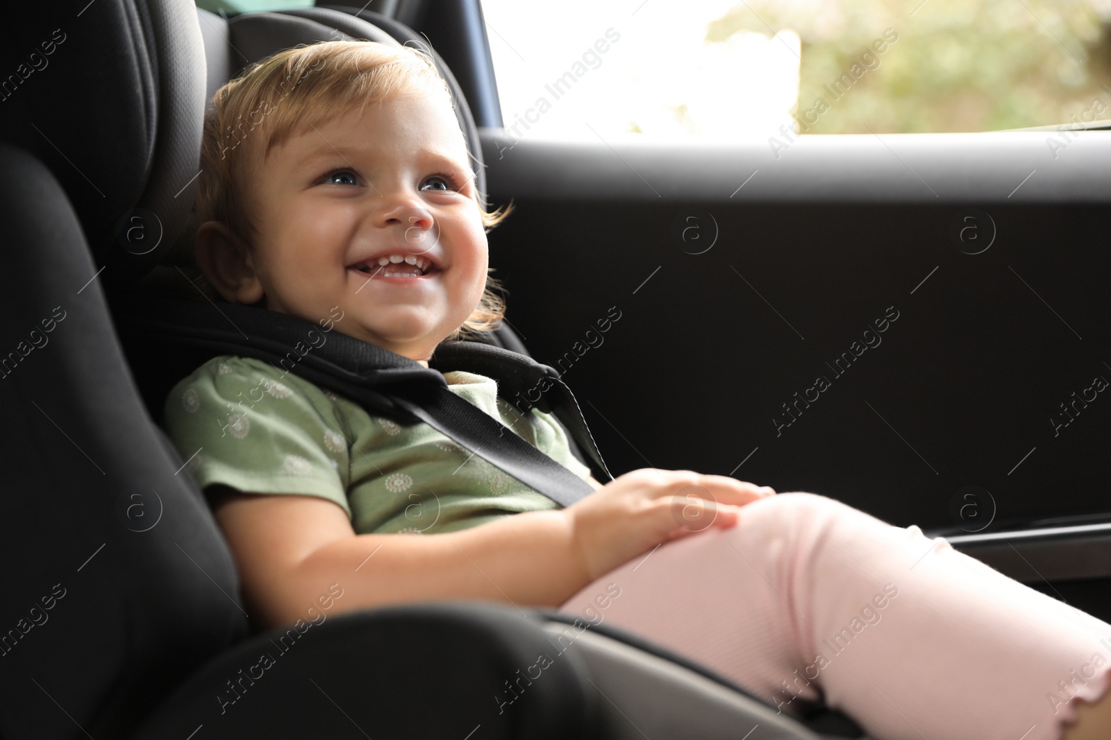 Photo of Cute little girl sitting in child safety seat inside car