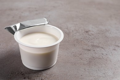 Photo of Plastic cup with delicious organic yogurt on grey table, closeup. Space for text