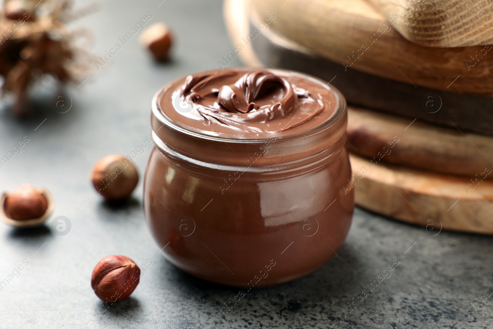 Photo of Glass jar with tasty chocolate hazelnut spread and nuts on grey table