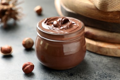 Glass jar with tasty chocolate hazelnut spread and nuts on grey table