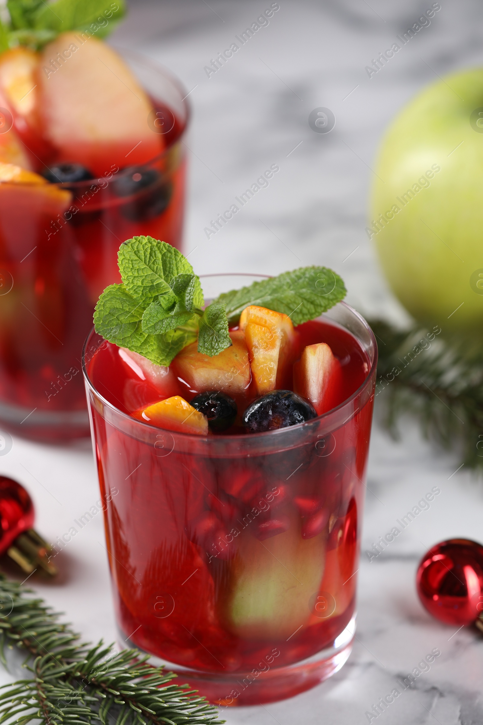 Photo of Aromatic Sangria drink in glasses, ingredients and Christmas decor on white marble table