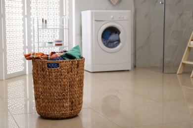 Photo of Wicker laundry basket full of different clothes on floor in bathroom