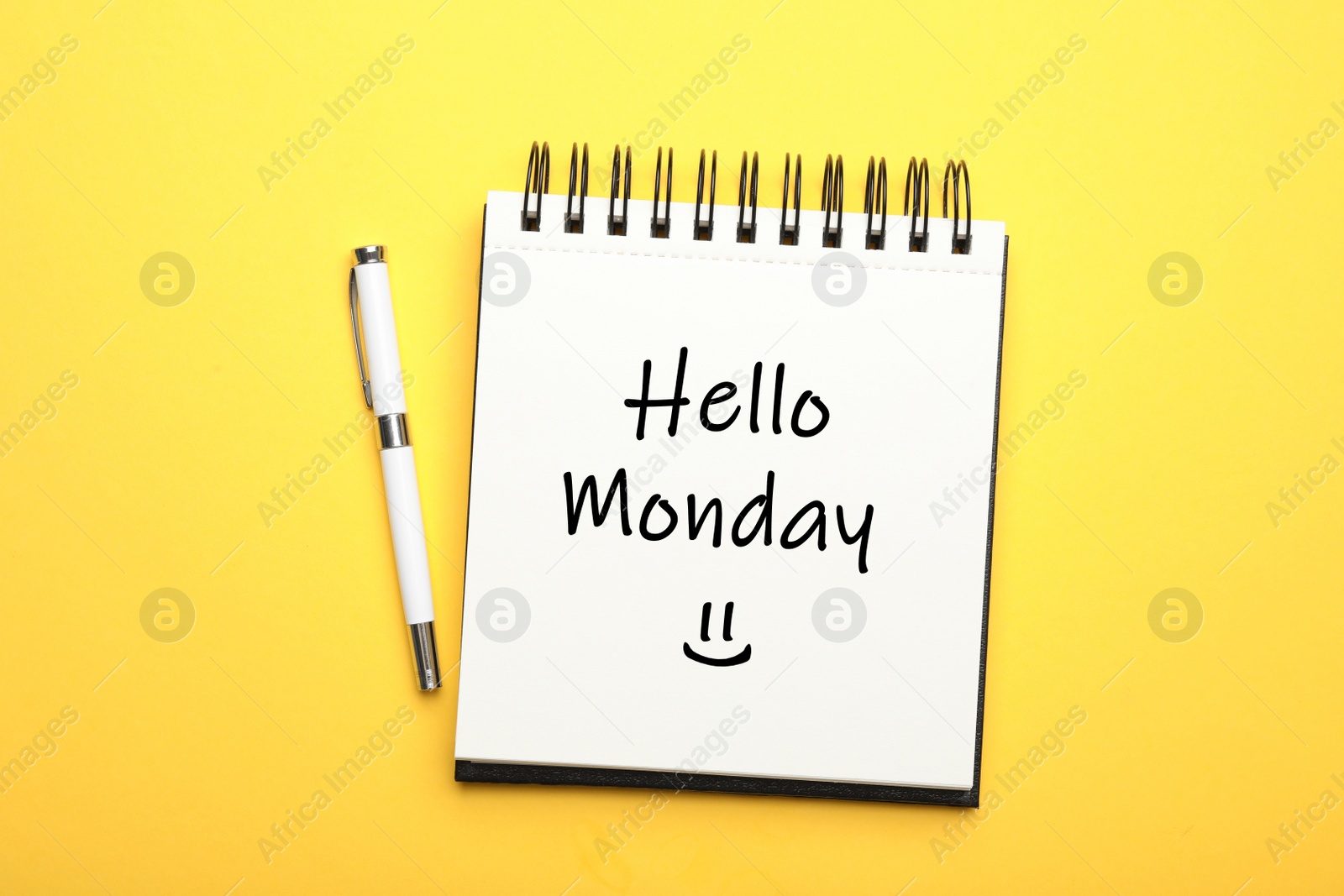 Image of Start your week with good mood. Open notebook with text Hello Monday and pen on yellow background, flat lay