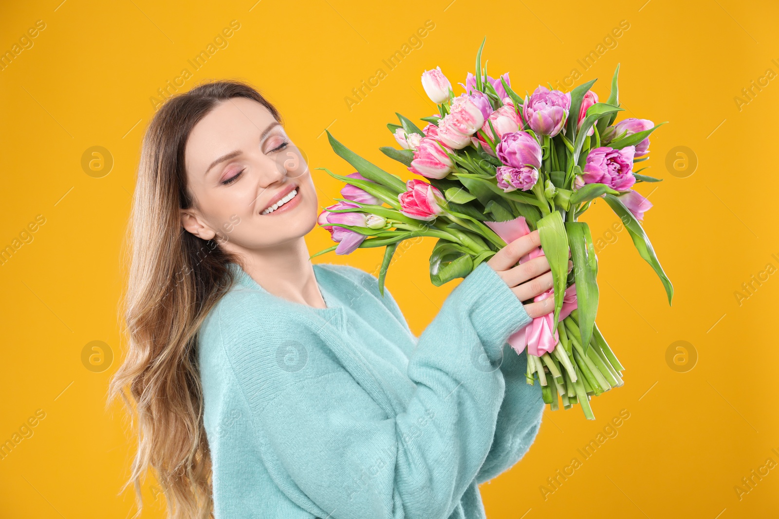 Photo of Happy young woman with bouquet of beautiful tulips on yellow background